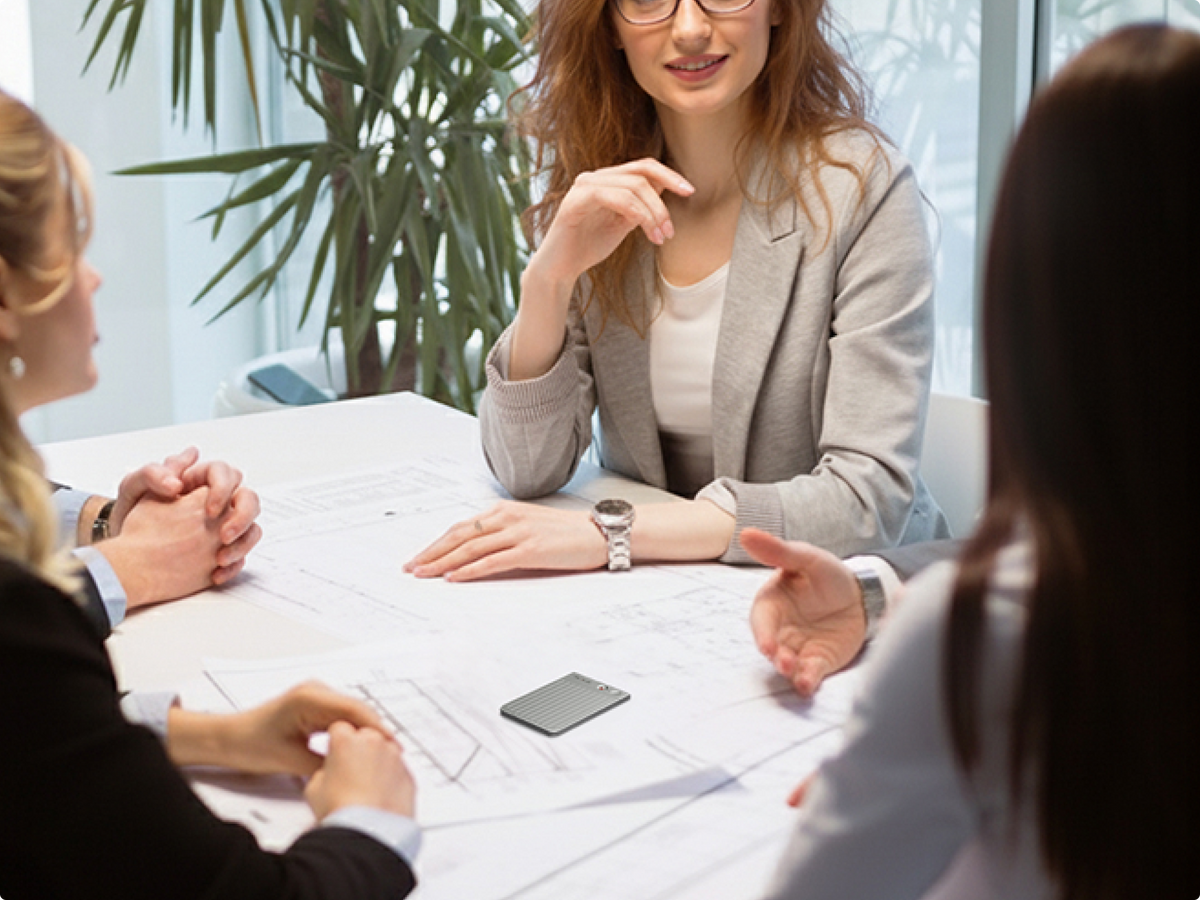 Professionals discuss blueprints in a meeting while a PLAUD NOTE AI voice recorder captures the conversation.