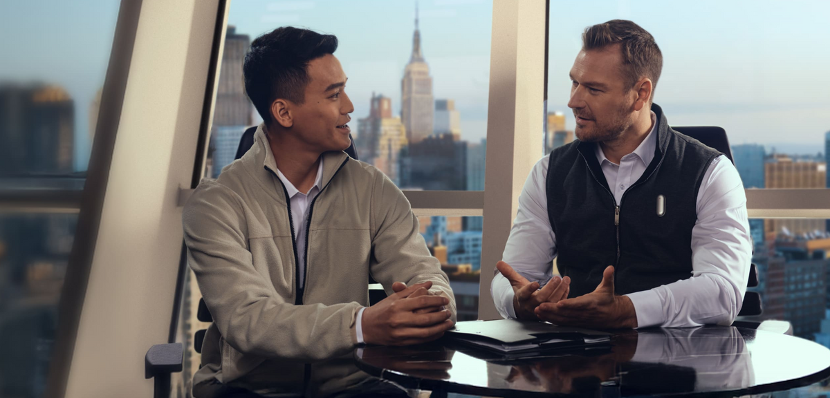 Two men in a business meeting, with one wearing a Plaud NotePin on his vest to record the conversation.