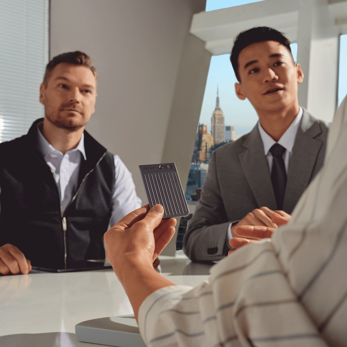 A professional holds the Plaud Note AI voice recorder during a business meeting in a modern office.