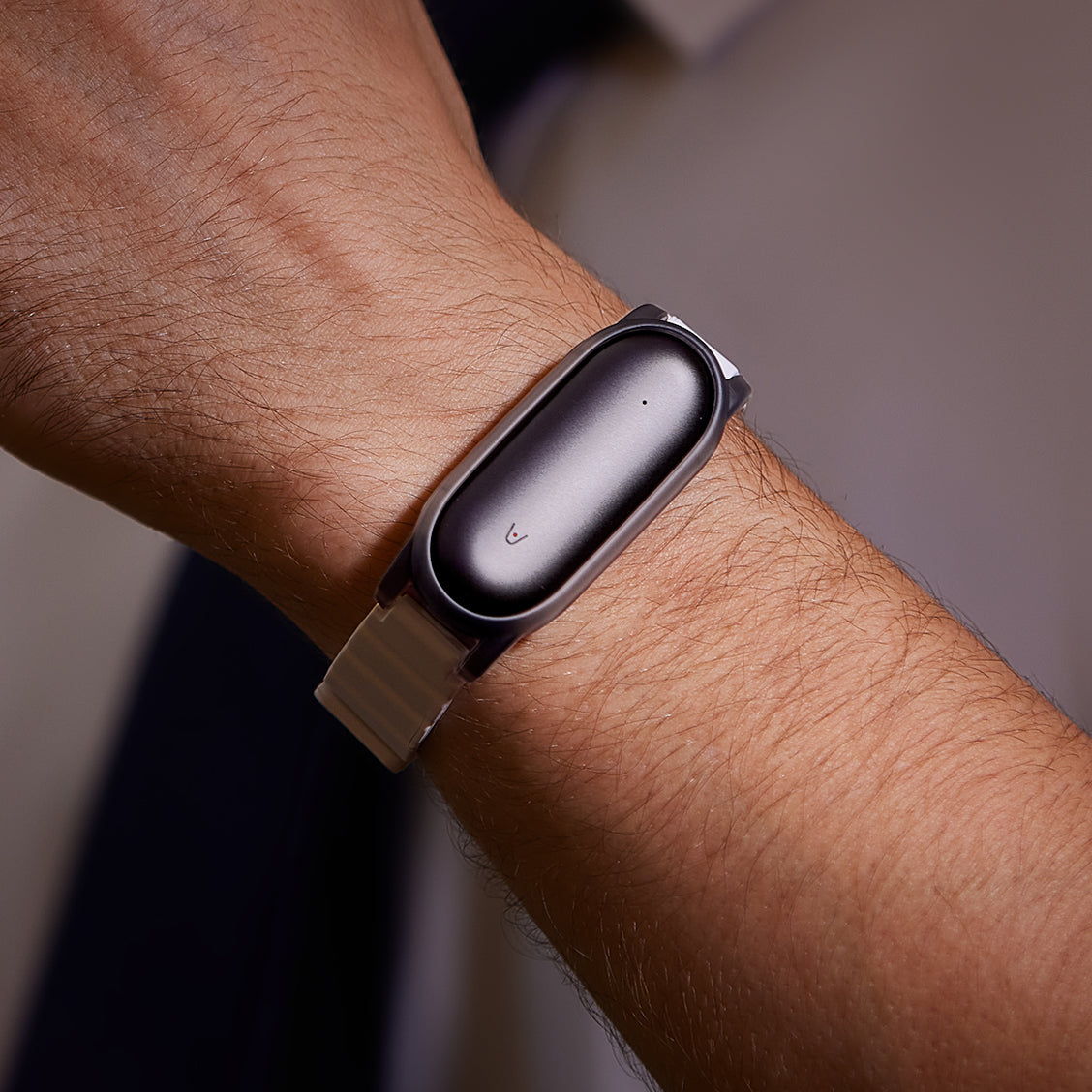 Close-up of the Plaud NotePin AI voice recorder worn on a wrist with a tan watch band.