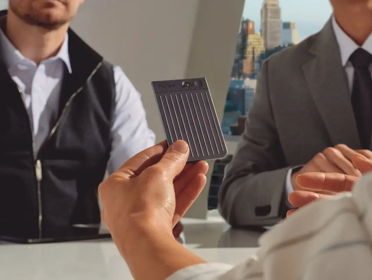 A person holds a grey Plaud Note AI voice recorder during a professional meeting in an office.