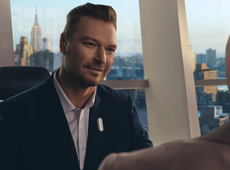 A businessman wearing the Plaud NotePin on his lapel during a meeting in a city office.