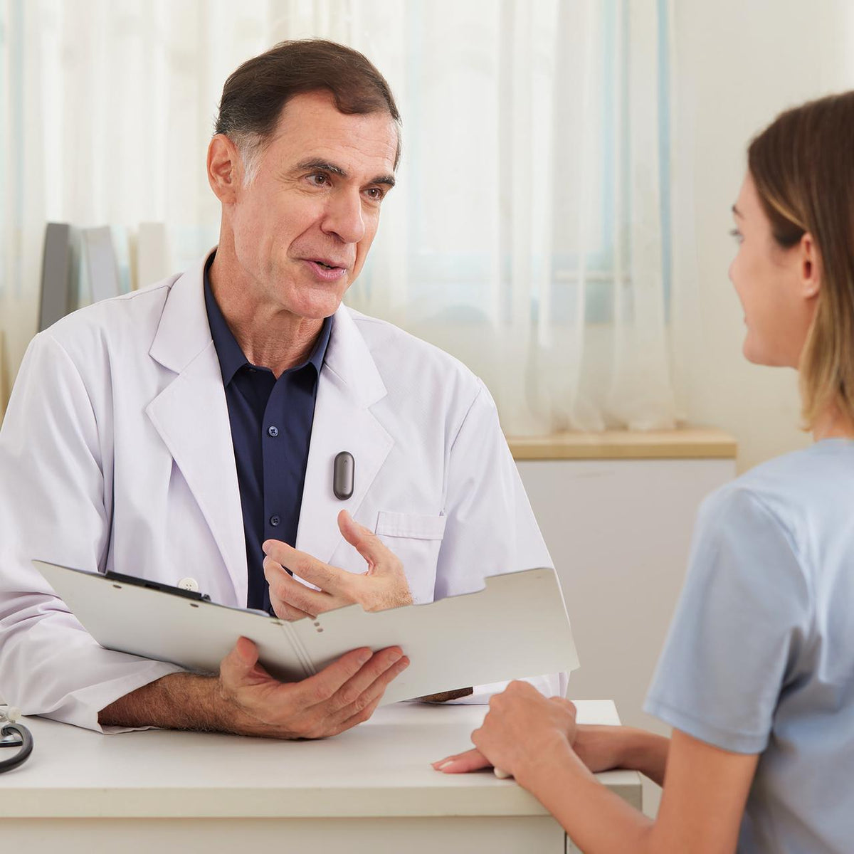 A doctor wearing a Plaud NotePin on his white coat while speaking with a patient during a consultation.