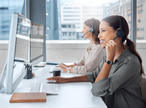 Smiling customer support representative wearing a headset while working at a computer in a modern office.