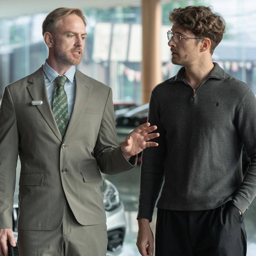 A man in a suit wearing a Plaud NotePin on his lapel while conversing with another man in a showroom.