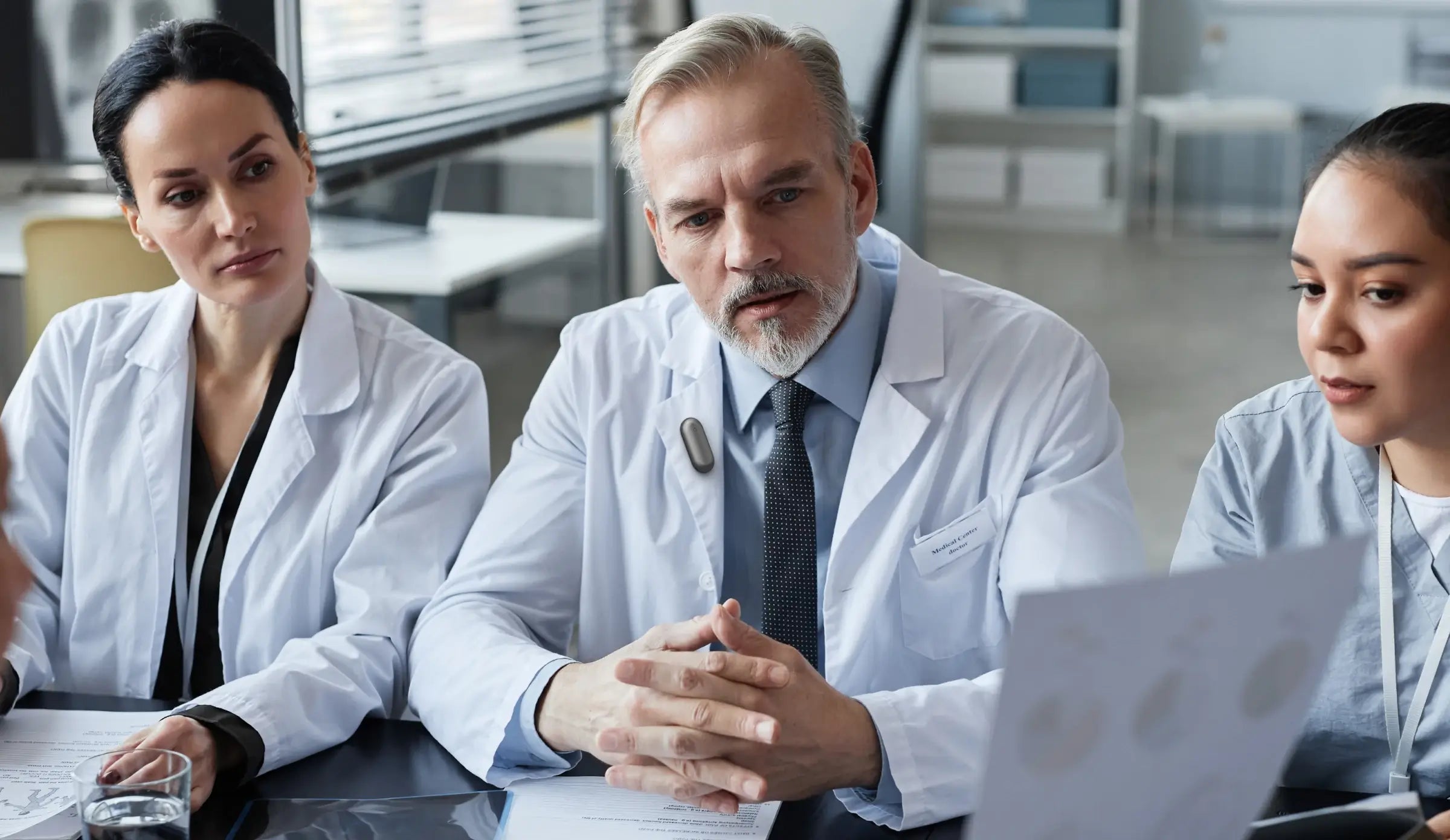 A doctor wearing the Plaud NotePin on his lapel during a professional medical consultation with colleagues.