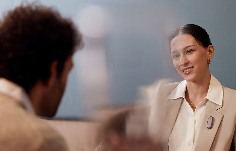A woman wearing the Plaud NotePin on her blazer lapel while engaged in a conversation.