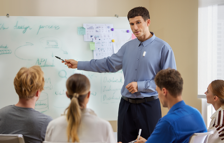 A man wearing a PLAUD NotePin leads a meeting, pointing to a whiteboard while recording the discussion.