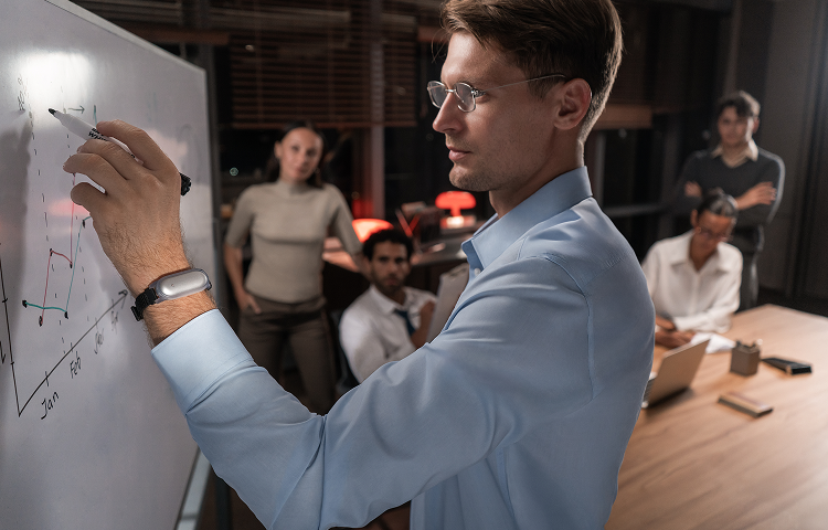 Professional wearing a PLAUD NotePin on his wrist while presenting a graph on a whiteboard to his team.