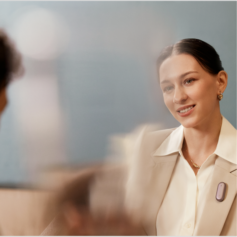 Professional woman wearing a Plaud NotePin AI voice recorder on her lapel during a meeting.