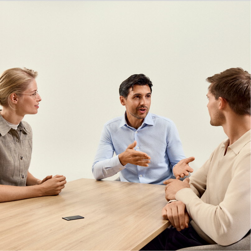 Three professionals discuss ideas around a table with a PLAUD NOTE AI voice recorder capturing the meeting.