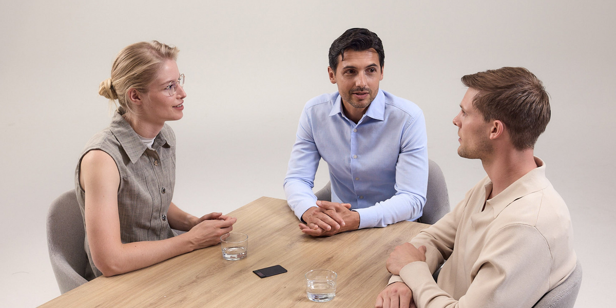Three colleagues in a discussion with a PLAUD NOTE AI recorder on the table to capture meeting notes.