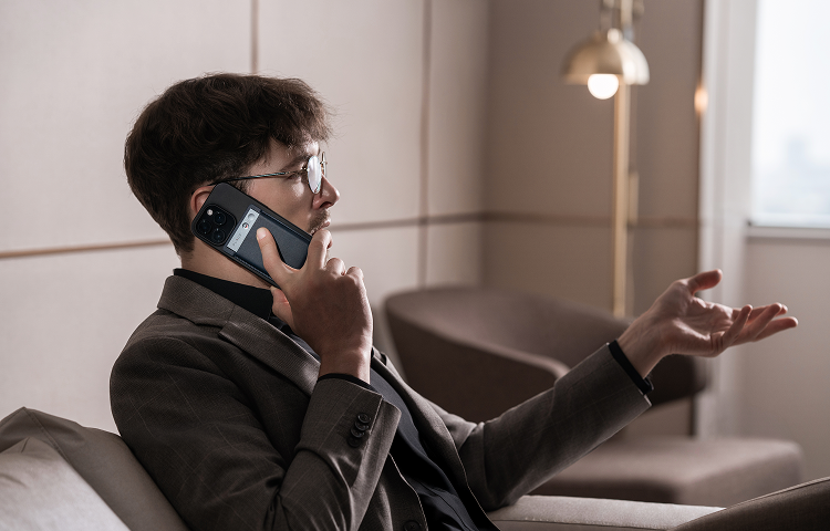 Man in a suit recording a phone call using the Plaud Note AI voice recorder attached to his smartphone.