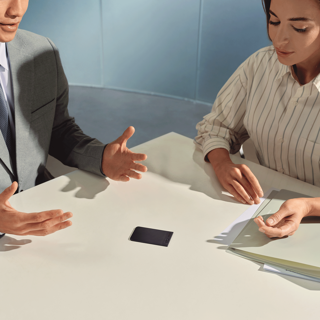 Two people in a business meeting with a Plaud Note voice recorder on the table capturing their conversation.