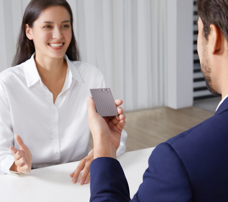A man holds a Plaud Note AI voice recorder during a professional meeting with a colleague.