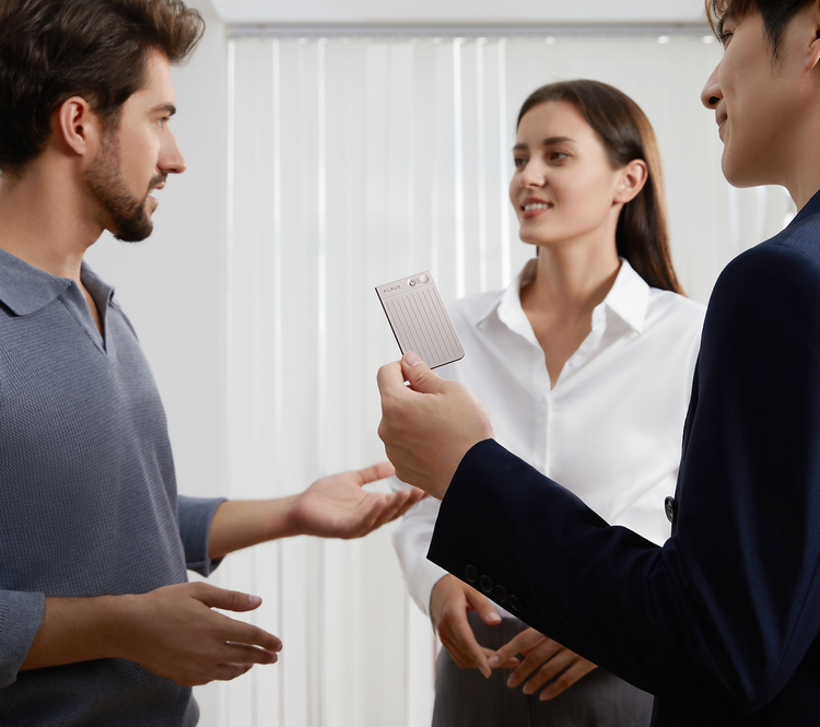 A professional holds a Plaud Note AI voice recorder during a business meeting with colleagues.