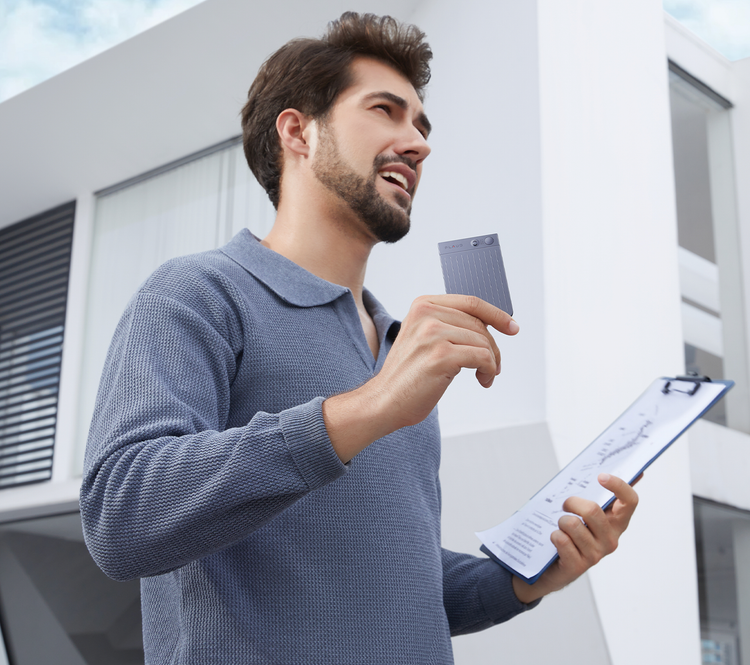 A man holding a clipboard and a Plaud Note AI voice recorder while standing outside a modern building.