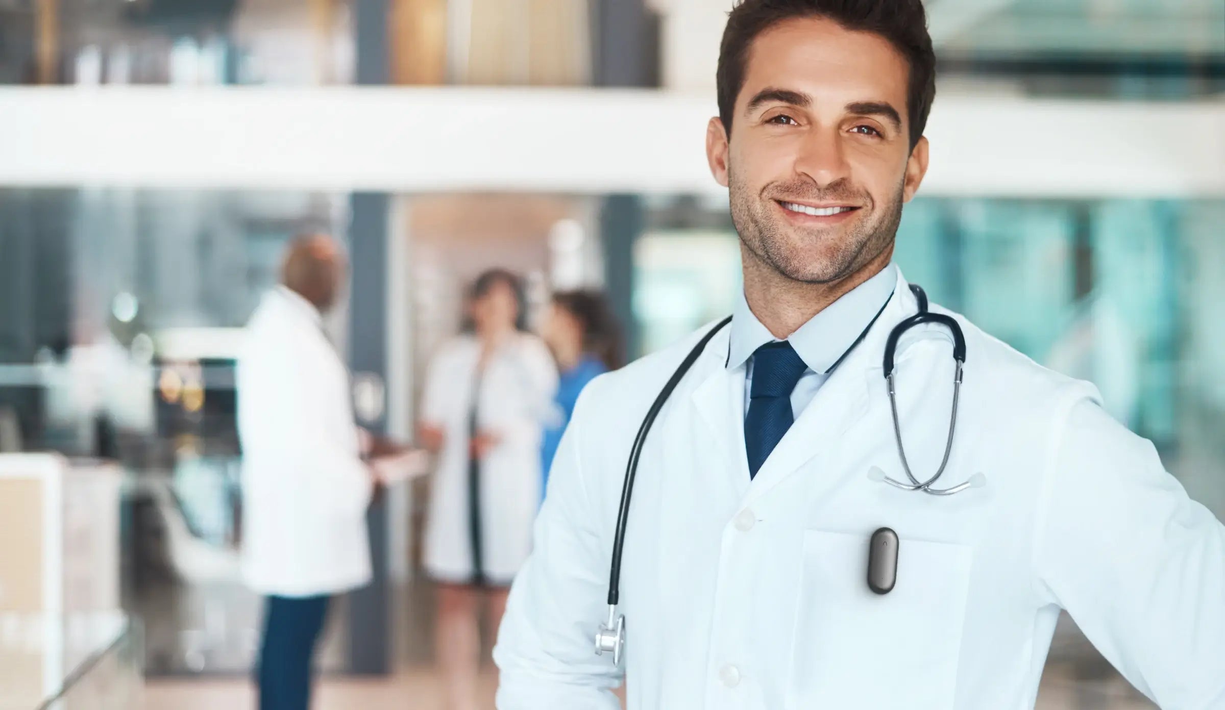 A smiling doctor wearing a Plaud NotePin AI voice recorder on his lab coat in a hospital setting.