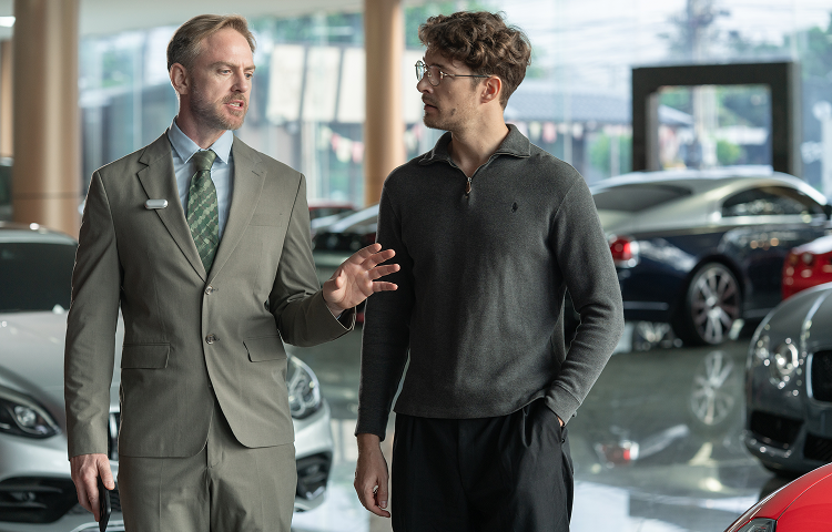 Professional wearing a Plaud NotePin on his lapel while talking to a client in a luxury car showroom.