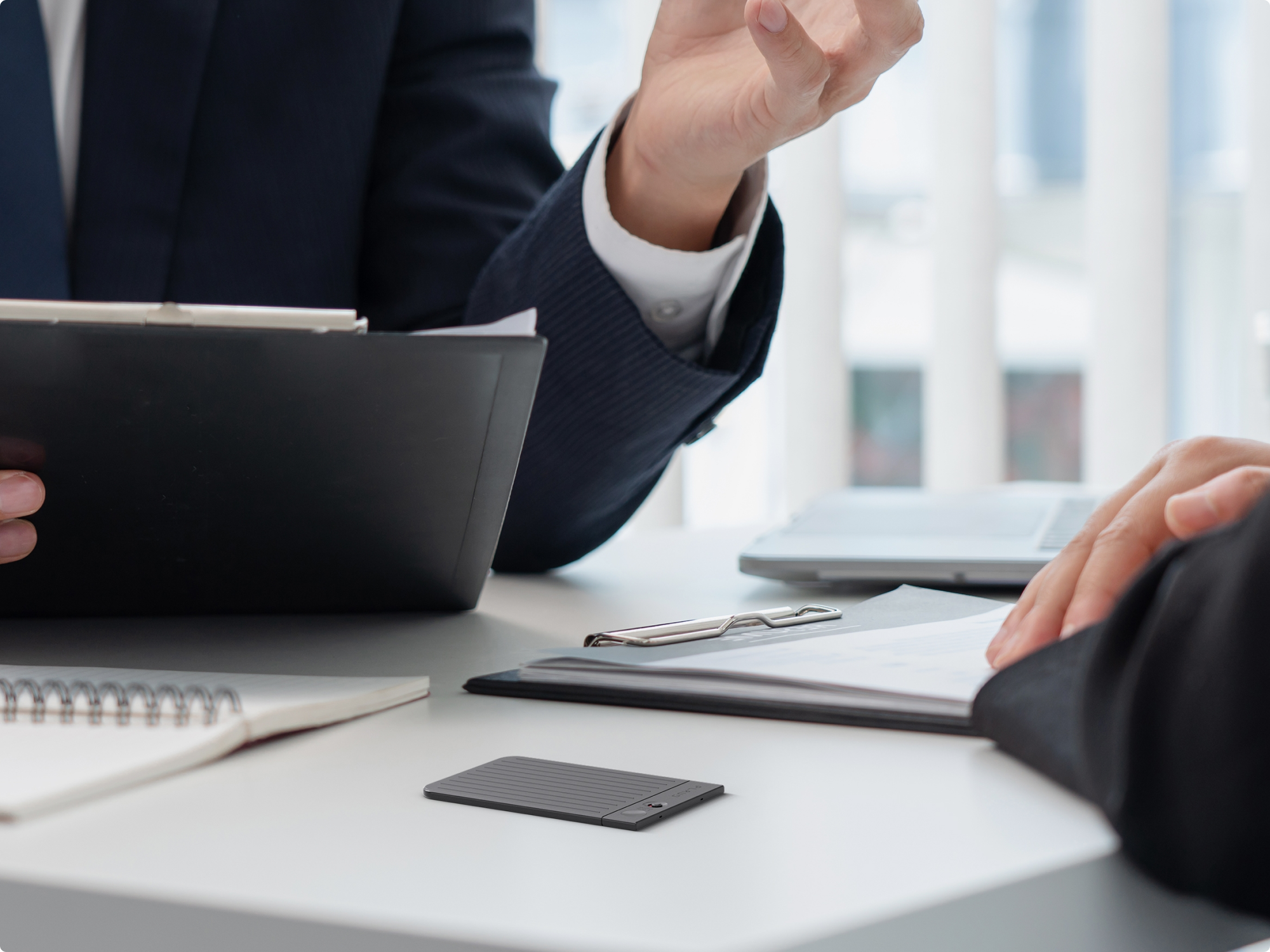 PLAUD NOTE AI voice recorder capturing a professional meeting between two business people in an office.