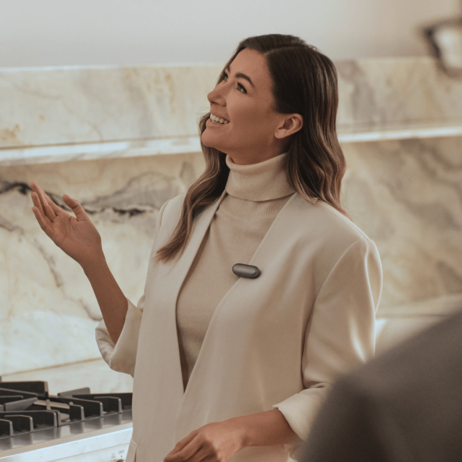 Woman wearing a Plaud NotePin AI voice recorder on her lapel while gesturing during a conversation.