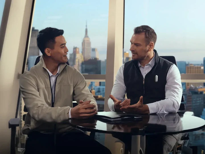 Two professionals in a meeting; one wears a Plaud NotePin on his vest to capture notes.