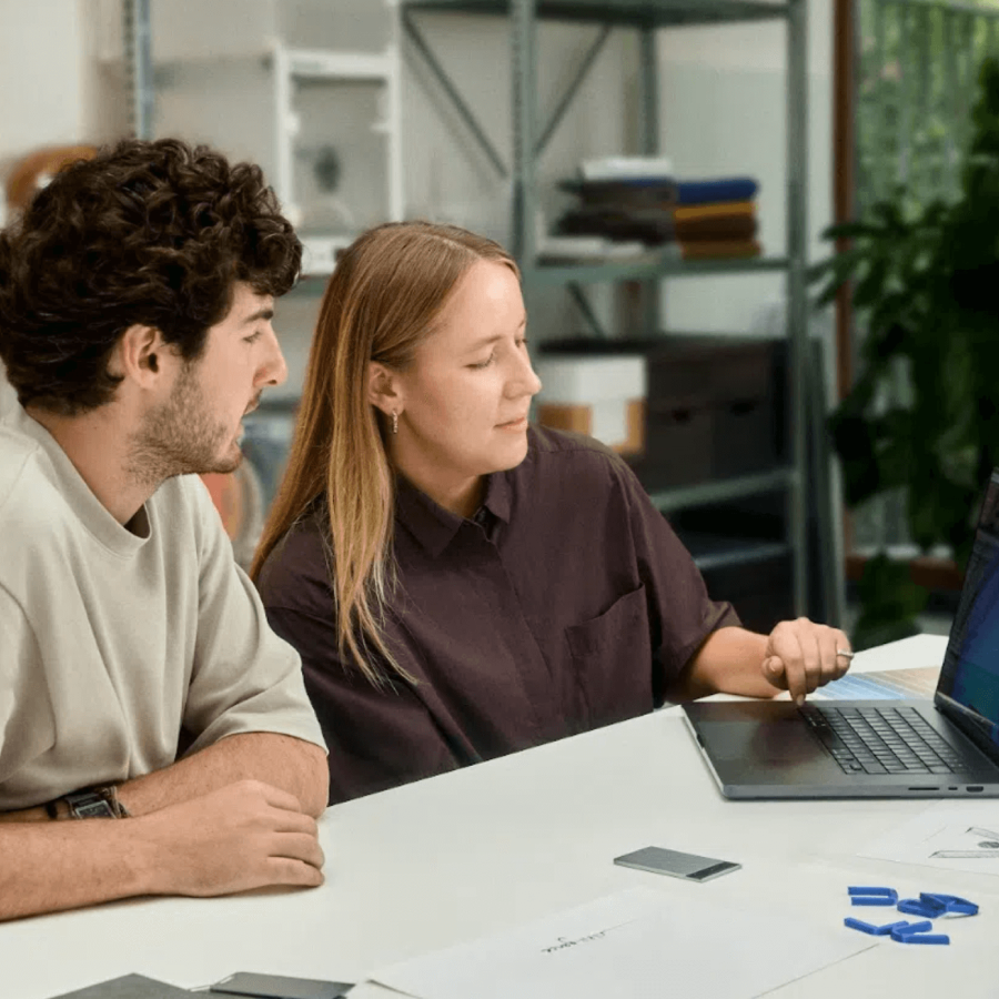 Two people review digital notes on a laptop with a Plaud Note AI voice recorder on the desk.