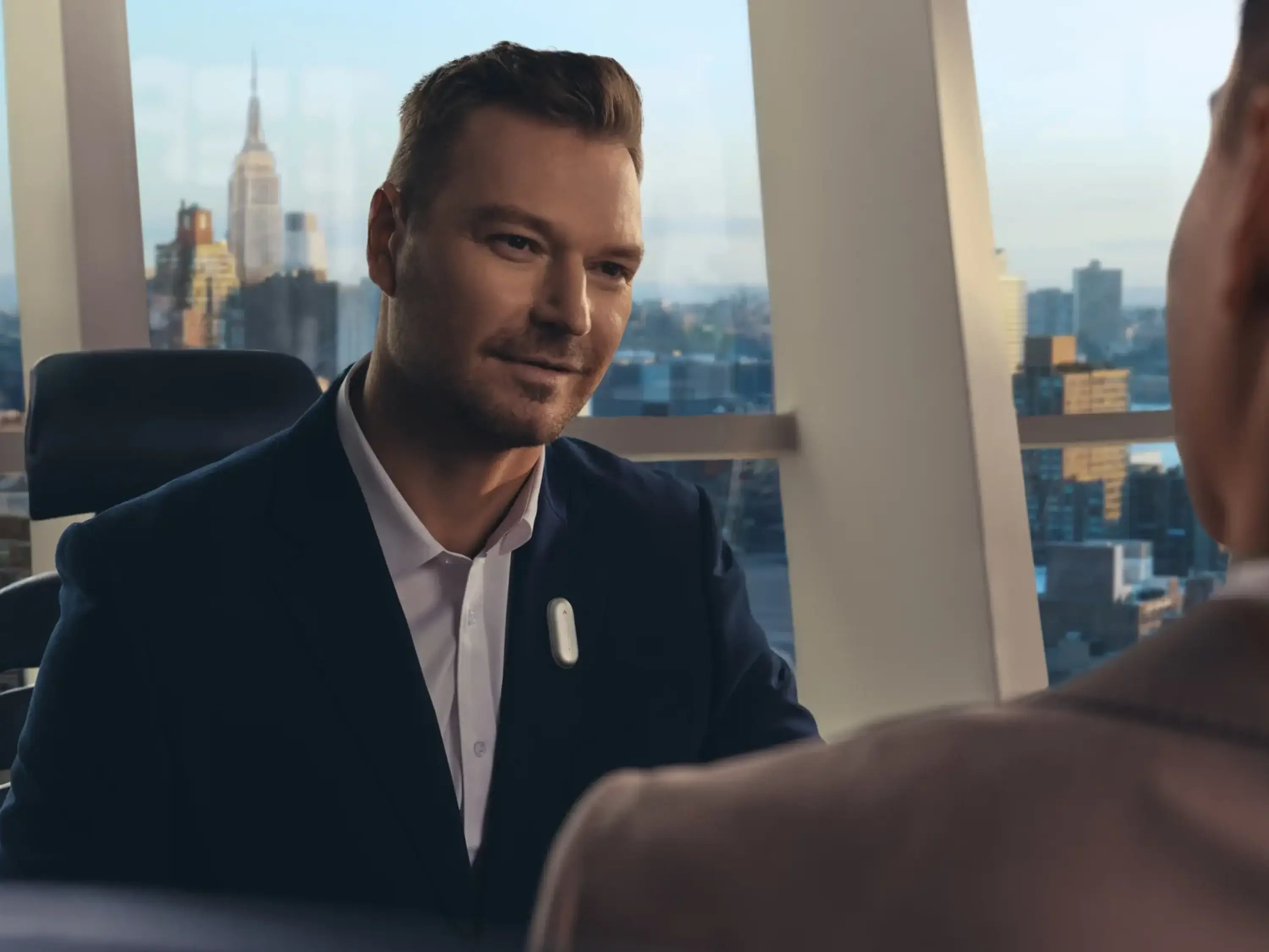 A professional man wearing a PLAUD NotePin during a business meeting in a high-rise office.