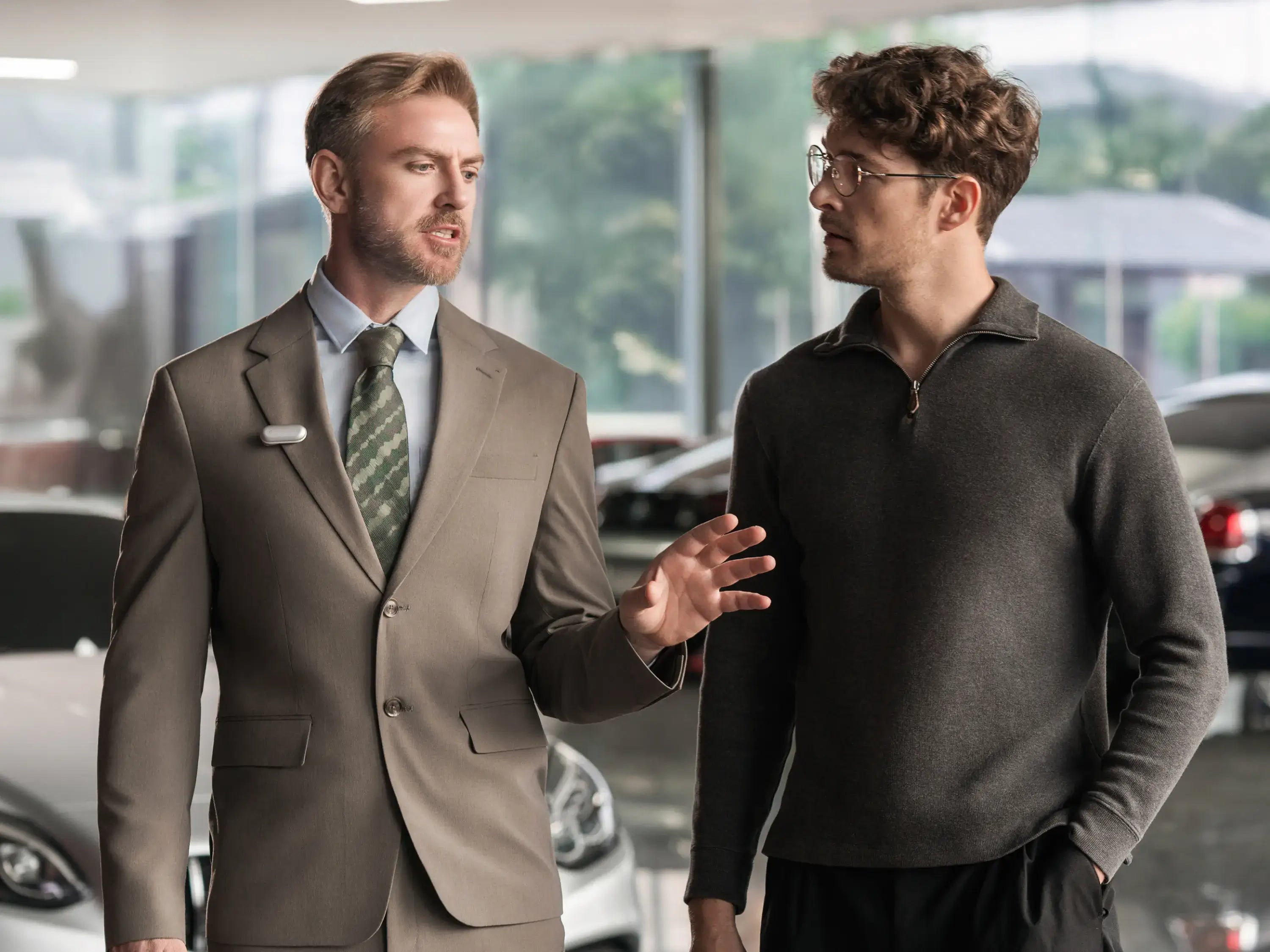 A professional wearing a Plaud NotePin on his lapel speaks with a client in a car showroom.