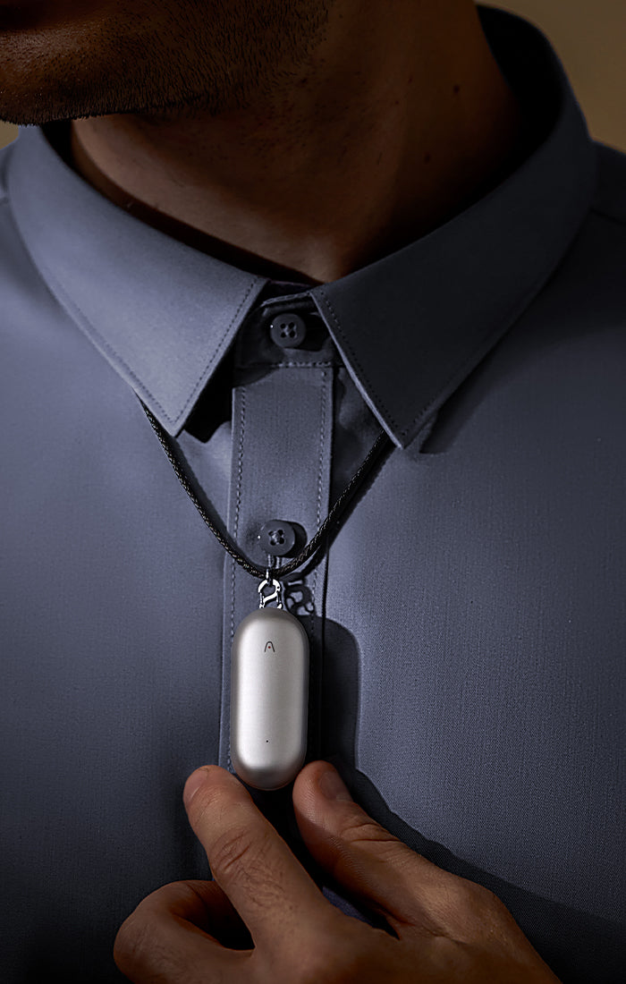 PLAUD NotePin AI voice recorder worn as a necklace by a person in a blue collared shirt.