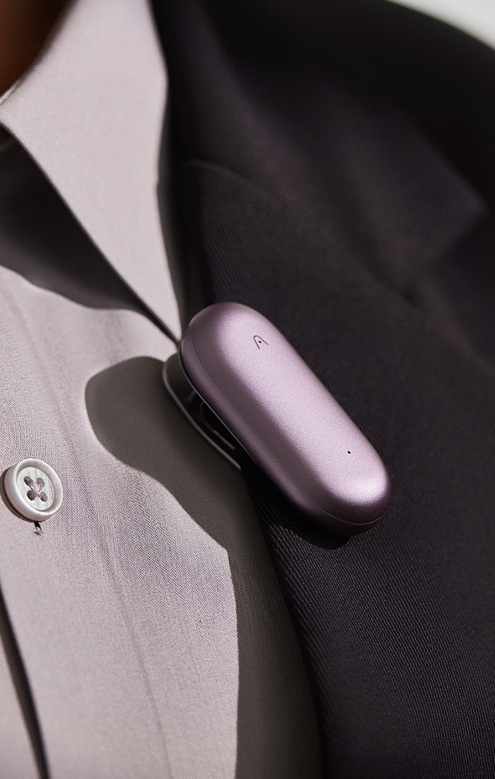 A purple PLAUD NotePin AI voice recorder clipped to the lapel of a dark suit jacket.