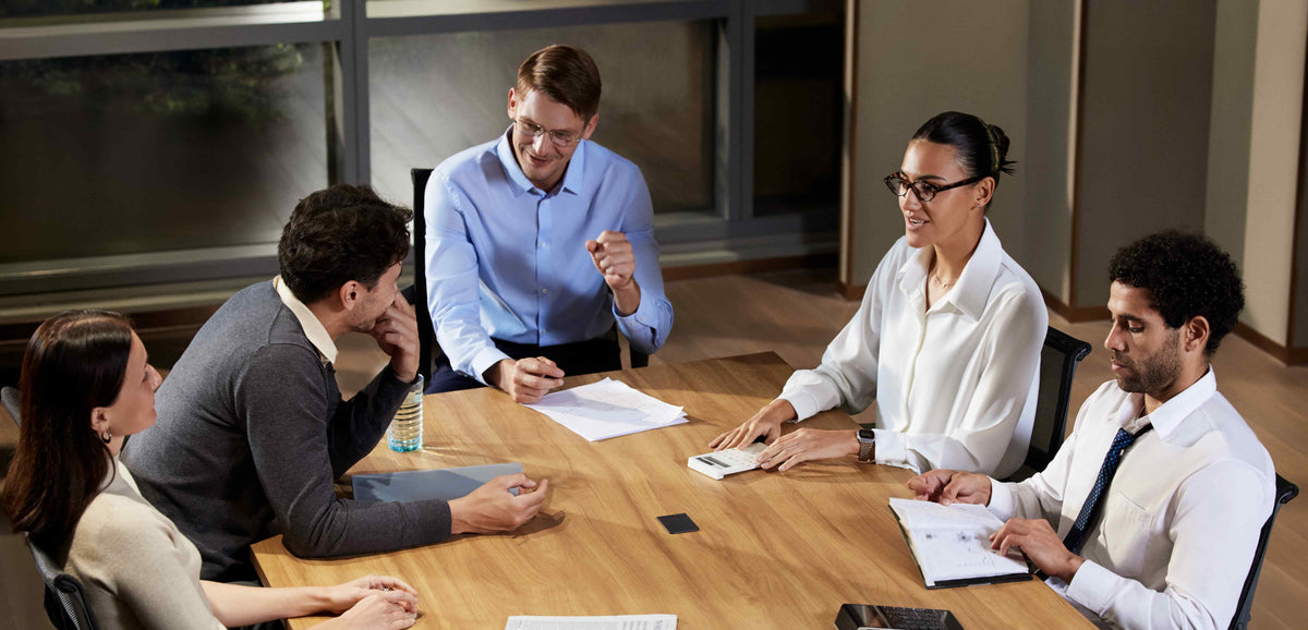 Professionals collaborate in a meeting with a PLAUD NOTE AI voice recorder placed on the table to capture notes.