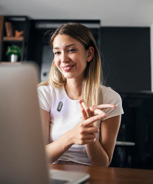 A woman wearing a Plaud NotePin on her shirt while using a laptop to record a meeting or conversation.