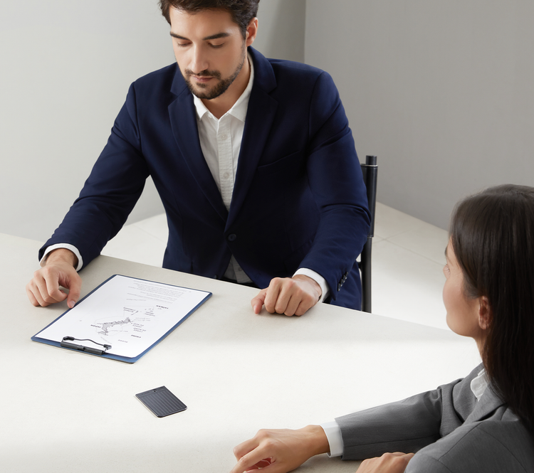 A man and woman in a business meeting with a PLAUD NOTE AI voice recorder on the table between them.