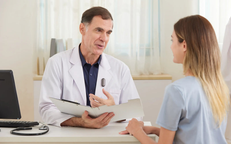 A doctor wearing a Plaud NotePin on his lapel while speaking with a patient during a medical consultation.