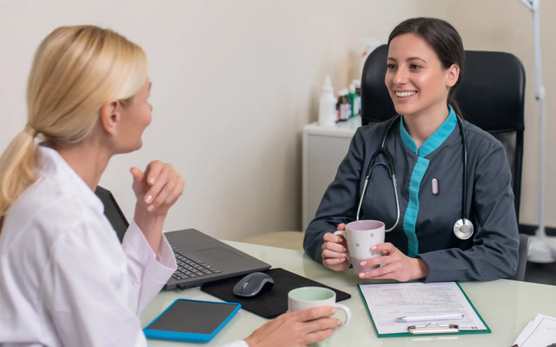 A healthcare professional wearing a Plaud NotePin on her scrubs while talking with a colleague in a medical office.