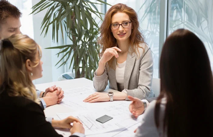 A PLAUD NOTE AI voice recorder sits on a table during a professional business meeting with four colleagues.