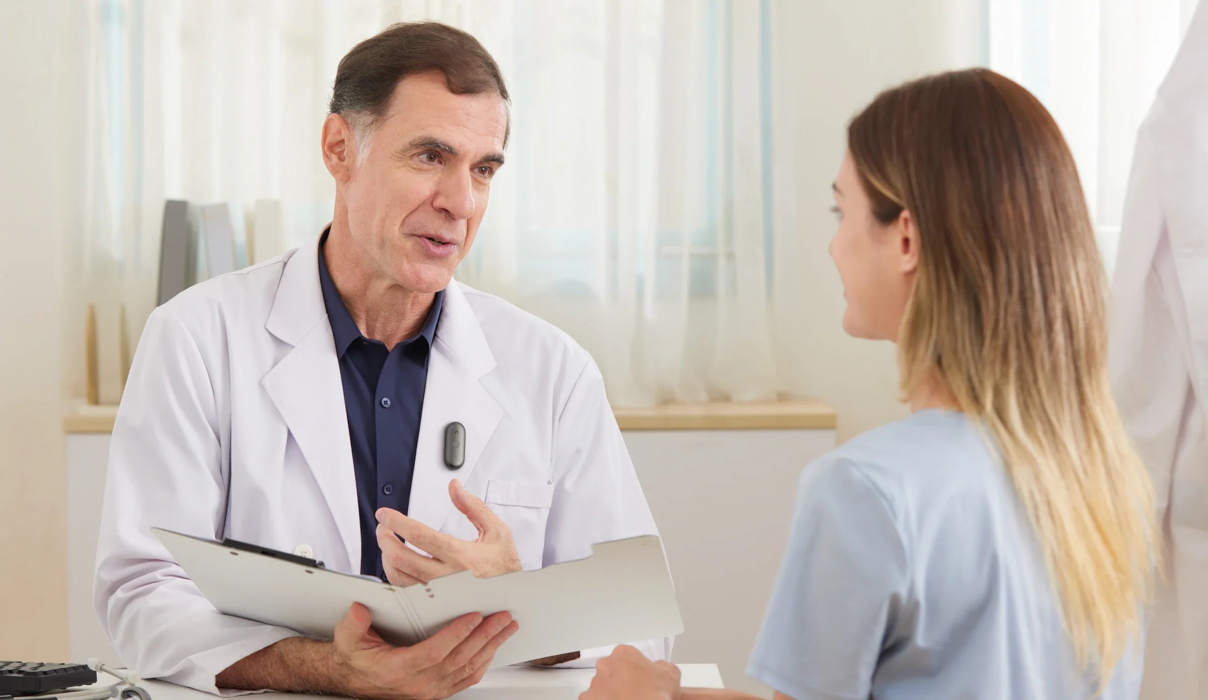 A doctor wearing a Plaud NotePin on his lab coat while consulting with a patient.