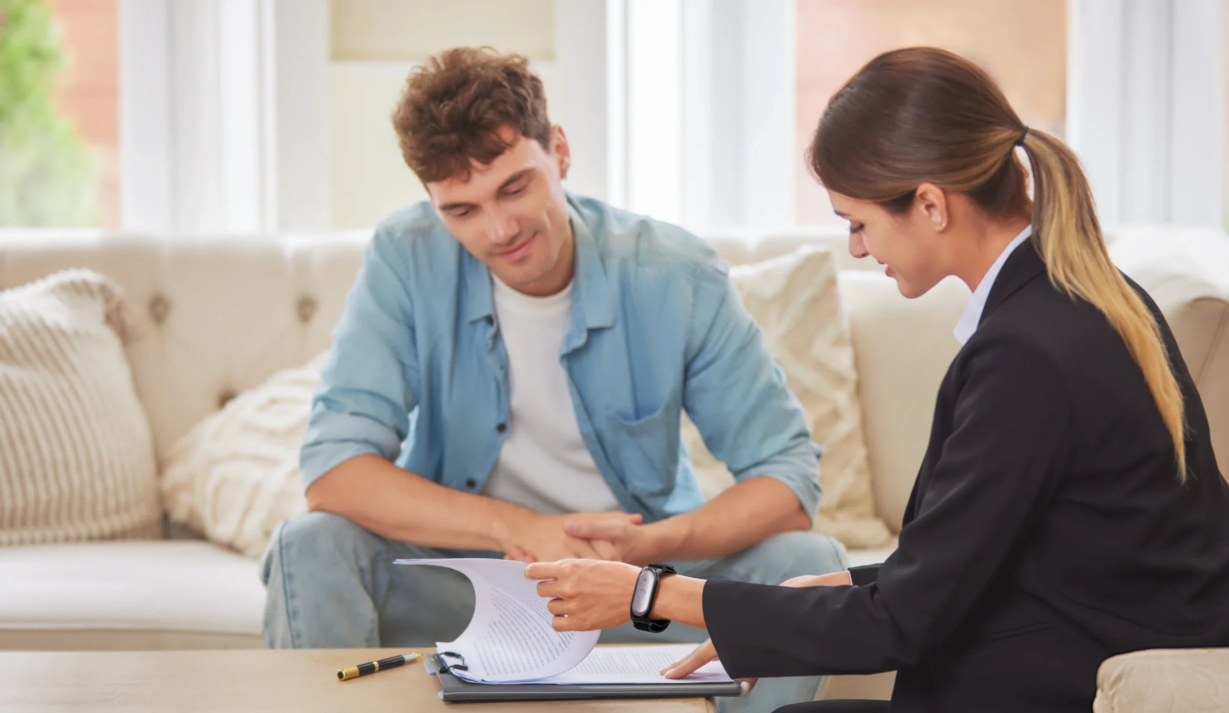 A professional woman wearing a Plaud NotePin on her wrist reviews documents during a meeting with a client.