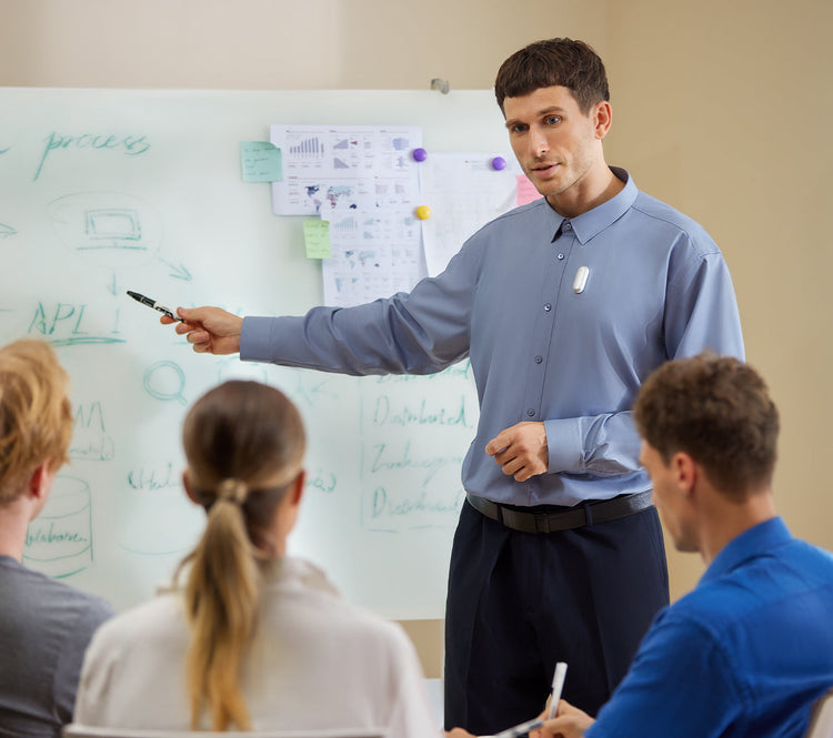 A presenter wearing a Plaud NotePin records a meeting while pointing to a whiteboard for his team.