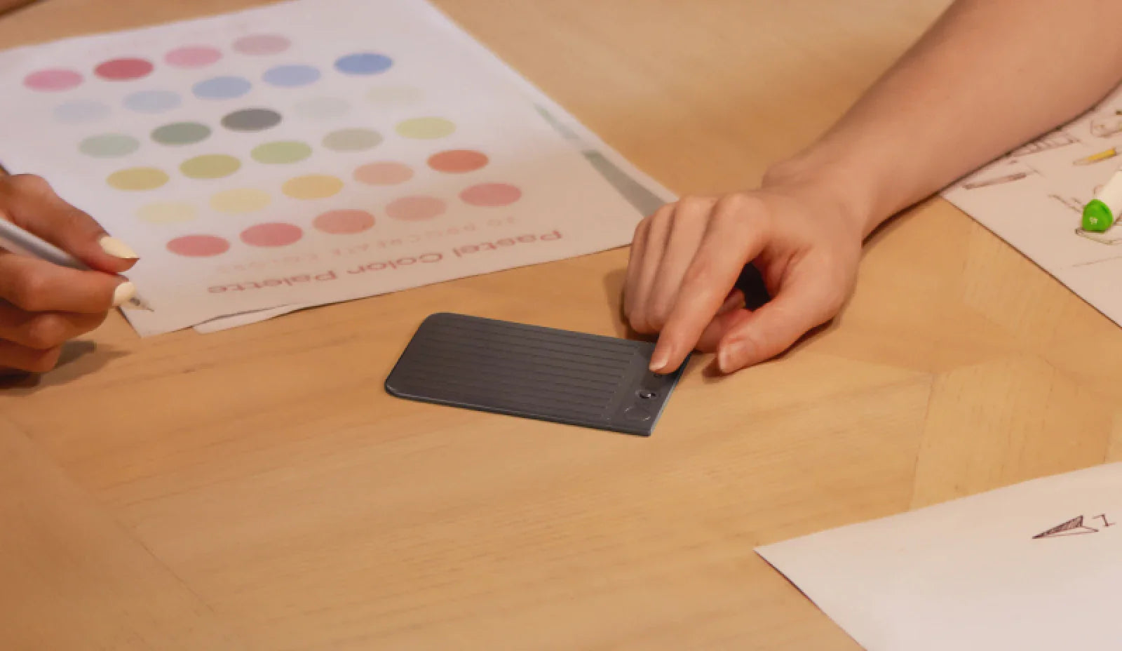 A person uses the slim Plaud Note AI voice recorder during a creative meeting with color palettes.