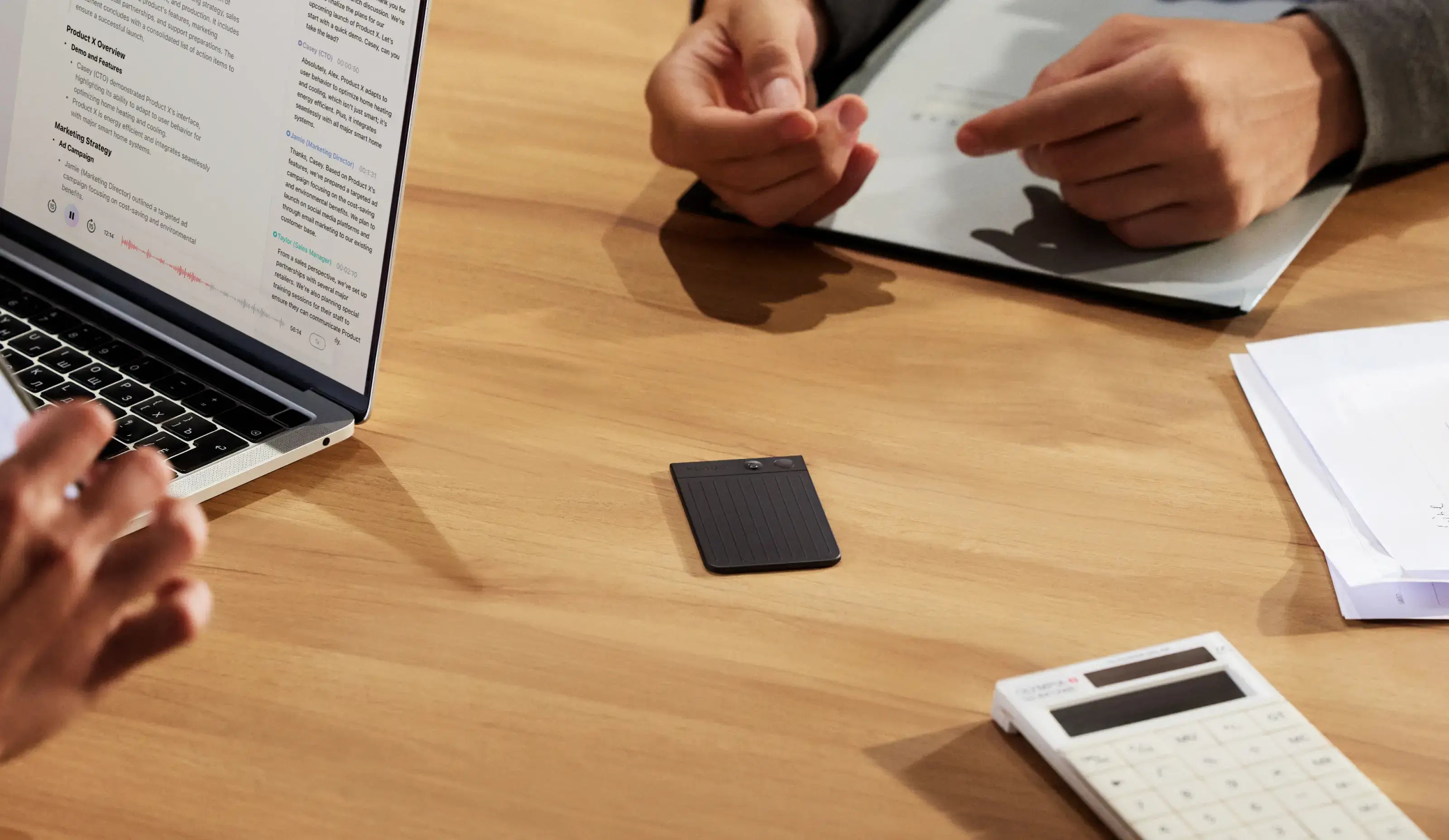 PLAUD NOTE AI voice recorder on a desk during a business meeting with a laptop displaying a transcript.