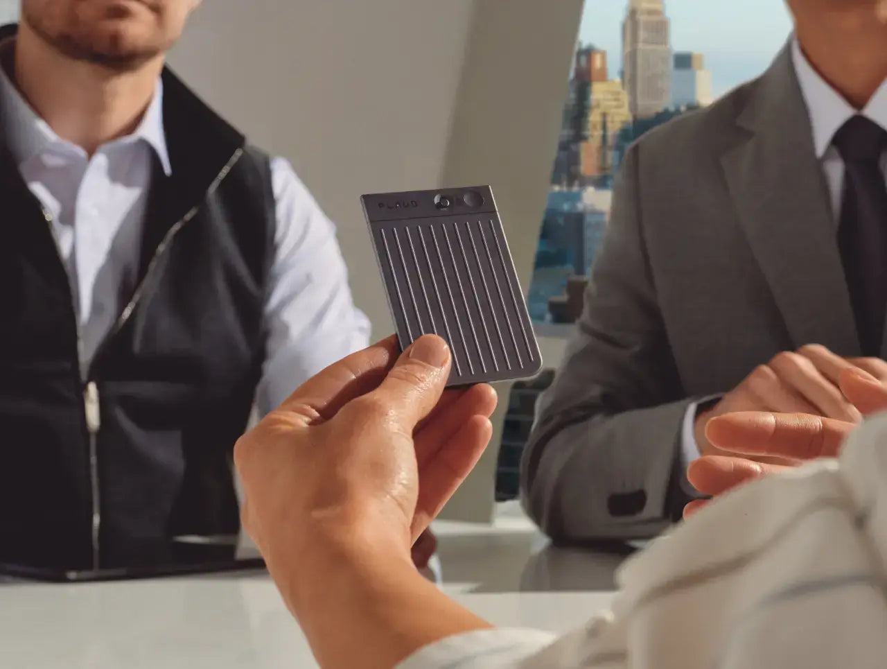 A person holds a grey Plaud Note AI voice recorder during a professional business meeting.
