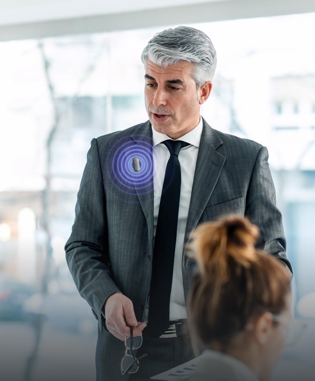 A businessman wearing a Plaud NotePin on his suit jacket to record a conversation during a meeting.