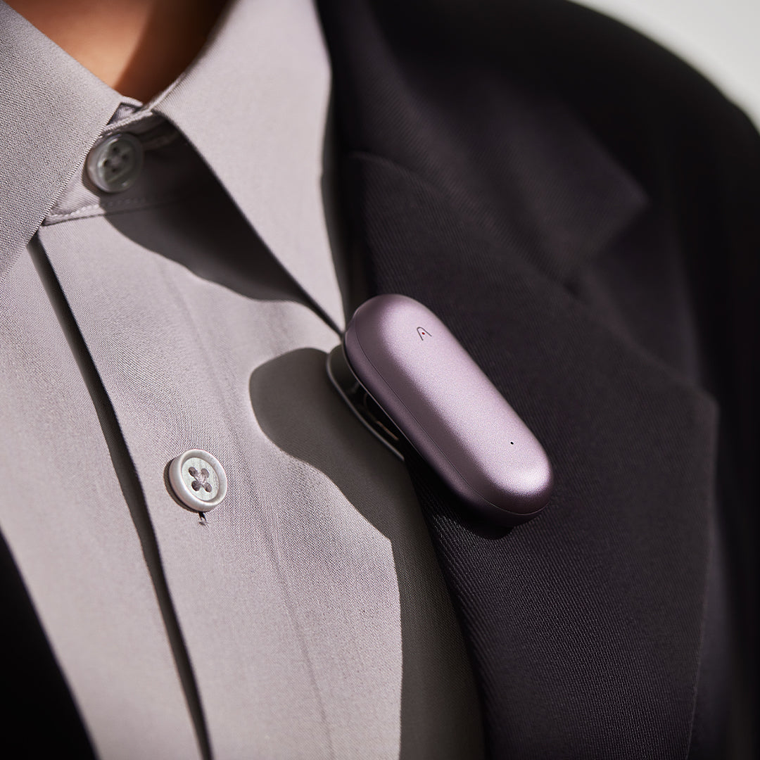 Purple Plaud NotePin AI voice recorder clipped to a person's blazer lapel.