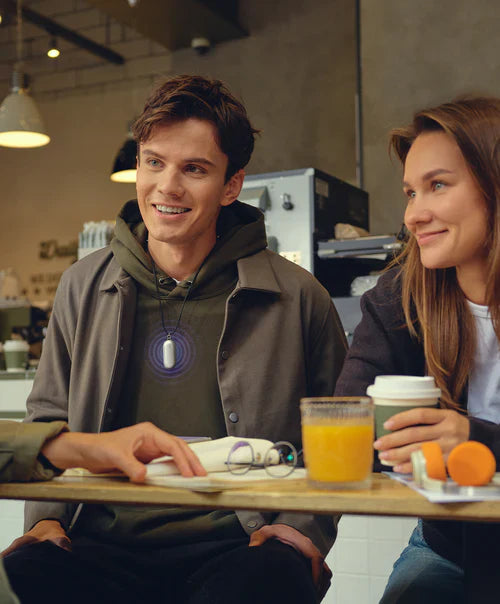 A man wears the Plaud NotePin as a necklace during a conversation at a cafe.