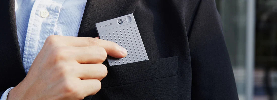 A person in a suit places the slim, grey PLAUD NOTE AI voice recorder into their blazer breast pocket.
