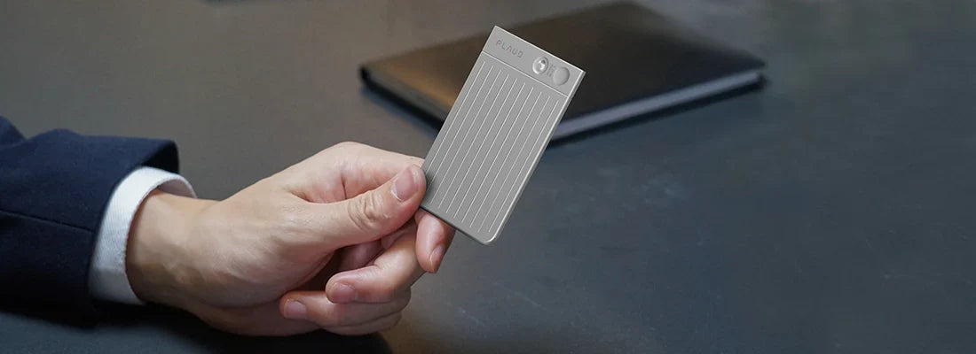 A person holding the silver PLAUD NOTE AI voice recorder, highlighting its slim and portable design.