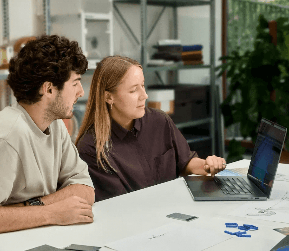 Two colleagues collaborating at a desk with a laptop and a PLAUD NOTE AI voice recorder.